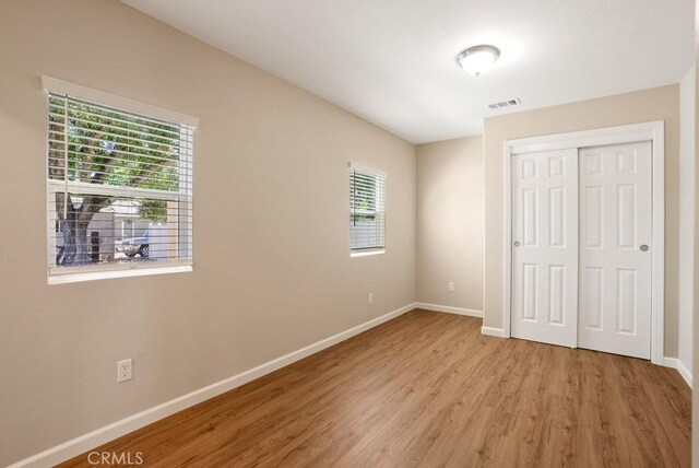 unfurnished bedroom with multiple windows, light wood-type flooring, and a closet