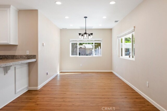 unfurnished dining area with an inviting chandelier and light hardwood / wood-style floors