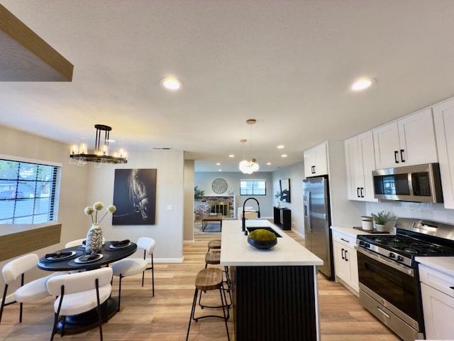 kitchen featuring a kitchen island with sink, decorative light fixtures, stainless steel appliances, and white cabinetry