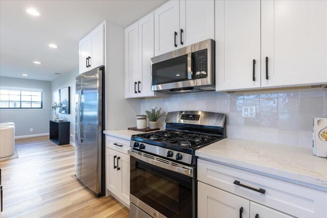 kitchen with tasteful backsplash, light wood-type flooring, appliances with stainless steel finishes, light stone countertops, and white cabinets