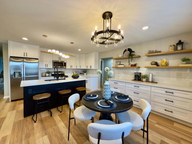 kitchen featuring sink, a center island with sink, hanging light fixtures, appliances with stainless steel finishes, and white cabinets