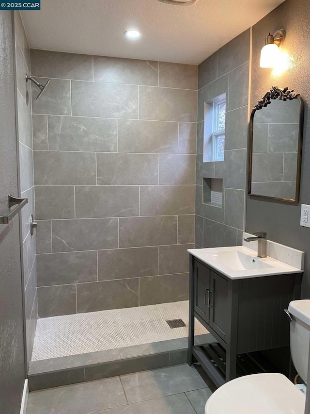 bathroom with vanity, tile patterned flooring, toilet, and tiled shower