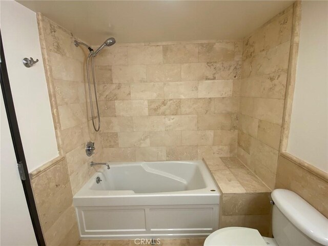 bathroom featuring tiled shower / bath combo, tile walls, and toilet