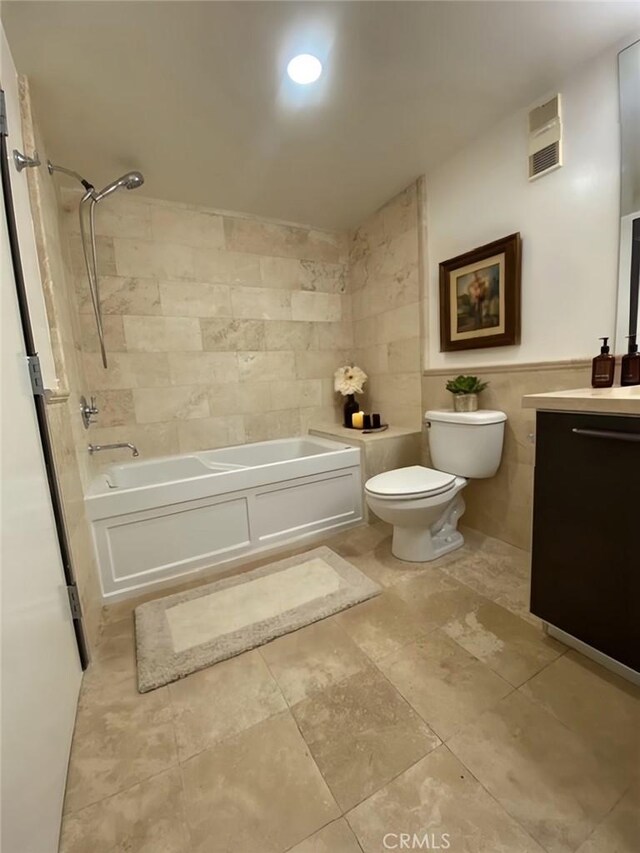 full bathroom featuring tiled shower / bath, vanity, toilet, and tile walls