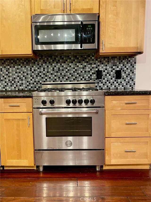 kitchen featuring appliances with stainless steel finishes, dark hardwood / wood-style floors, dark stone countertops, and decorative backsplash