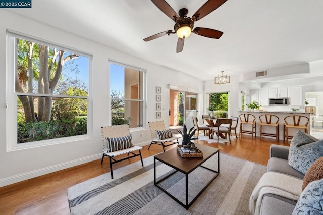 living room featuring ceiling fan with notable chandelier, light hardwood / wood-style floors, and a healthy amount of sunlight