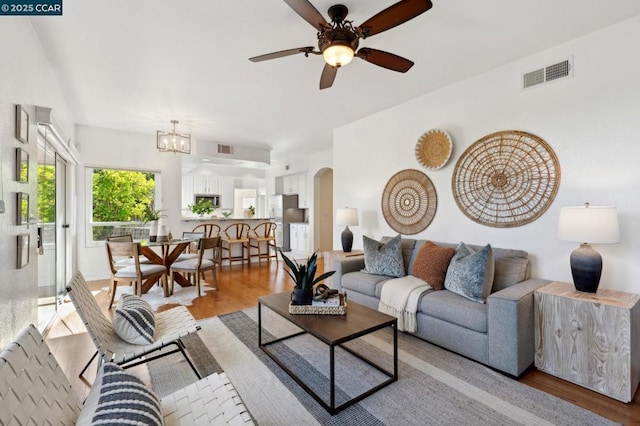 living room featuring ceiling fan with notable chandelier and light hardwood / wood-style flooring