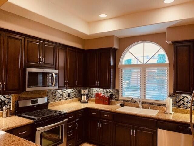 kitchen with tasteful backsplash, appliances with stainless steel finishes, light stone countertops, and sink