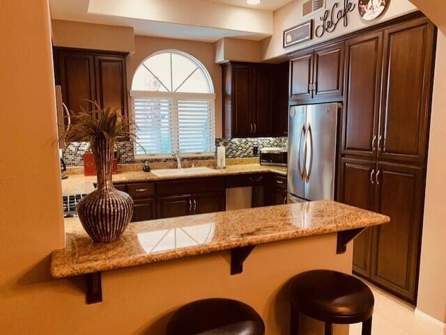 kitchen with a breakfast bar, sink, stainless steel refrigerator, and kitchen peninsula