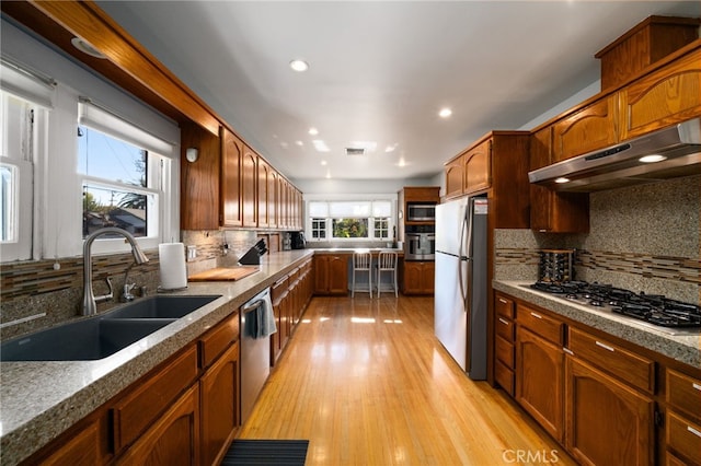 kitchen with tasteful backsplash, appliances with stainless steel finishes, sink, and light wood-type flooring