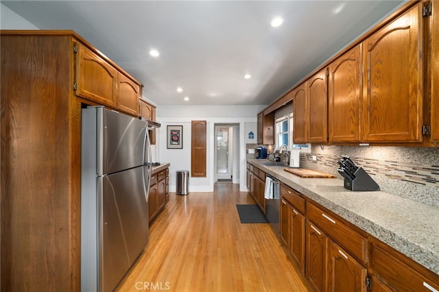 kitchen with sink, appliances with stainless steel finishes, backsplash, light stone countertops, and light wood-type flooring