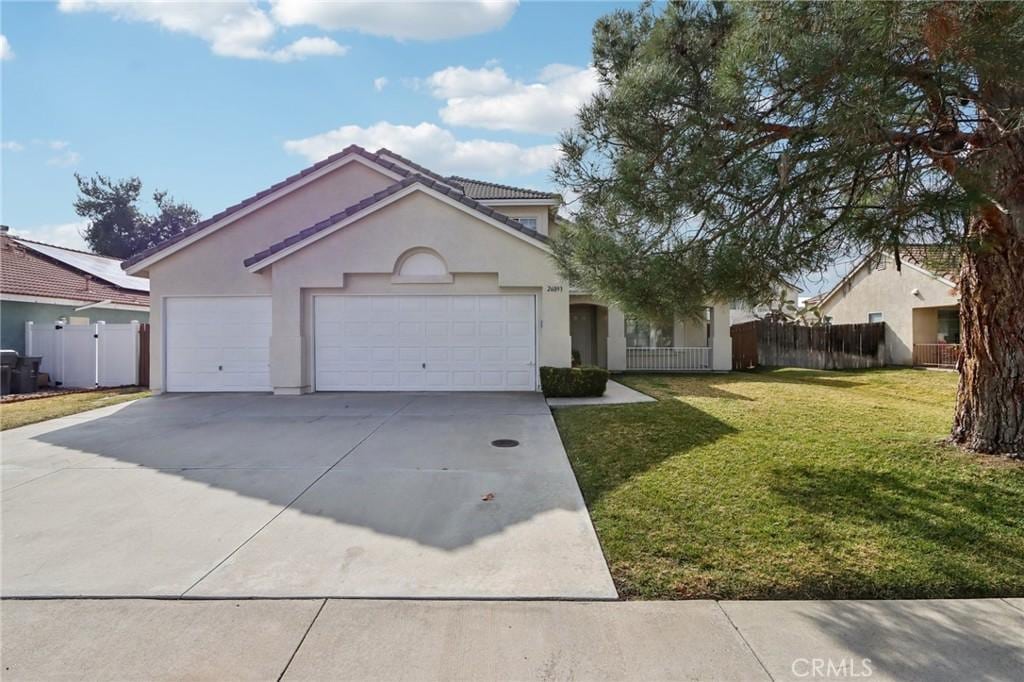 view of front facade with concrete driveway, stucco siding, an attached garage, fence, and a front yard