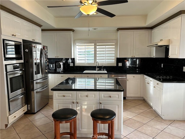 kitchen with appliances with stainless steel finishes, light tile patterned floors, white cabinets, a kitchen island, and sink