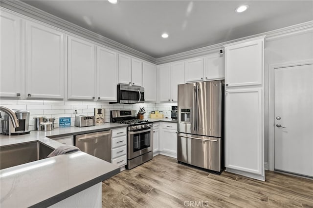 kitchen featuring appliances with stainless steel finishes, tasteful backsplash, sink, white cabinets, and light hardwood / wood-style flooring