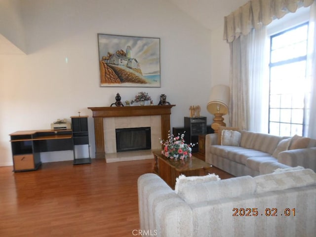 living room with lofted ceiling, plenty of natural light, wood-type flooring, and a tile fireplace