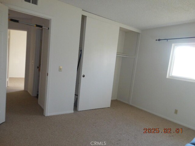 unfurnished bedroom featuring light colored carpet, a closet, and a textured ceiling