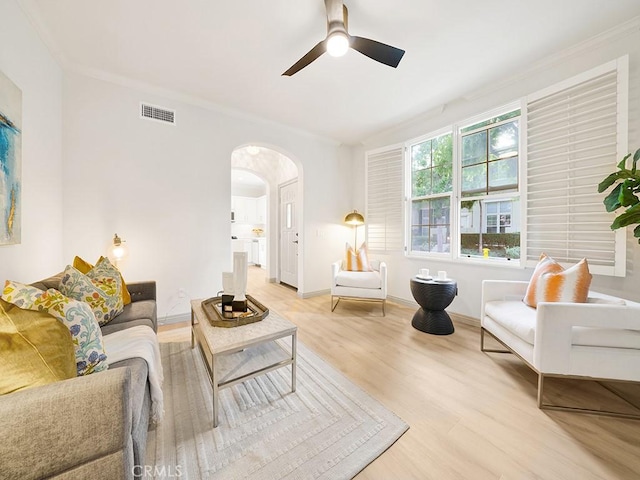 living area featuring arched walkways, visible vents, wood finished floors, ceiling fan, and crown molding