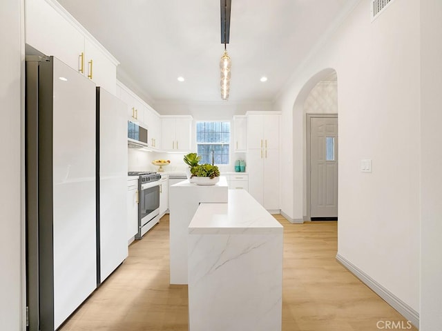 kitchen featuring white cabinetry, hanging light fixtures, stainless steel gas range oven, a kitchen island, and white fridge