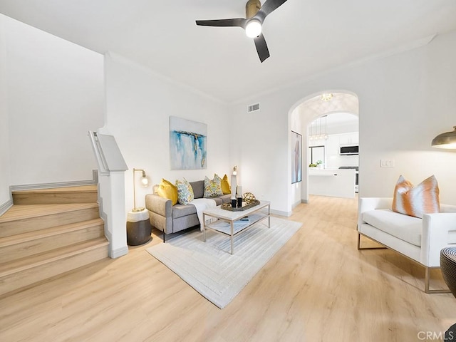 living room with light wood-type flooring, ceiling fan, arched walkways, baseboards, and visible vents
