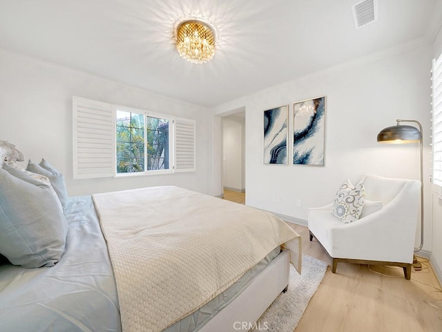 bedroom with an inviting chandelier, crown molding, and light hardwood / wood-style flooring