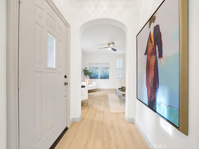 corridor with light wood-type flooring, baseboards, and arched walkways