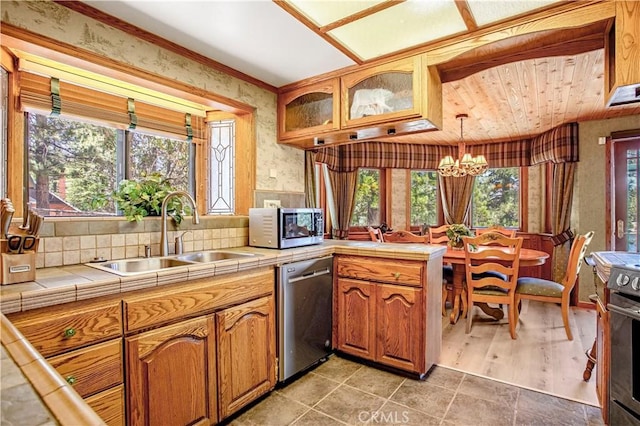 kitchen with tile countertops, sink, hanging light fixtures, stainless steel appliances, and a healthy amount of sunlight