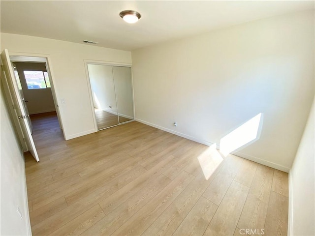 unfurnished bedroom featuring baseboards, a closet, visible vents, and light wood-style floors