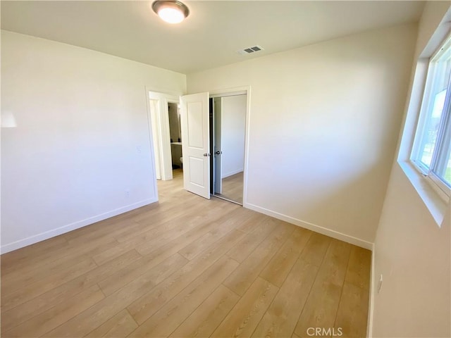 empty room featuring light wood-type flooring, visible vents, and baseboards