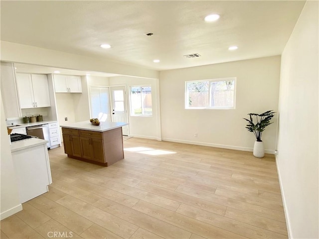 kitchen featuring a kitchen island, white cabinetry, light countertops, dishwasher, and light wood finished floors