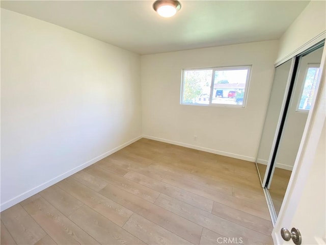 unfurnished bedroom featuring light wood-style flooring, baseboards, and a closet