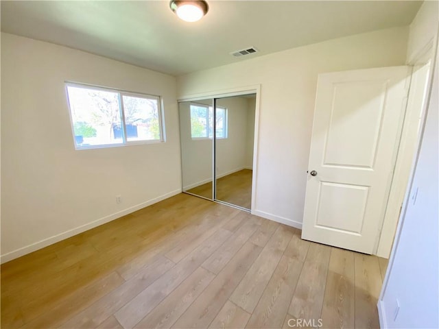 unfurnished bedroom with light wood finished floors, visible vents, baseboards, and a closet