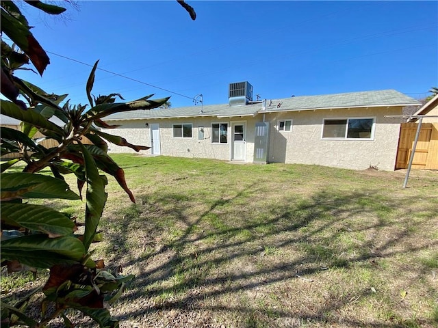 rear view of property with a lawn, fence, central AC unit, and stucco siding