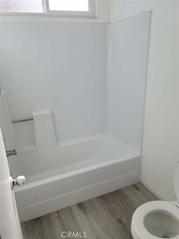 bathroom with wood-type flooring, tub / shower combination, and toilet