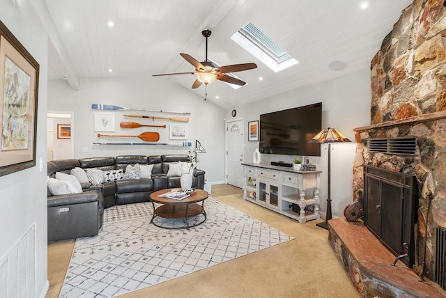 carpeted living room featuring a stone fireplace, lofted ceiling with skylight, and ceiling fan