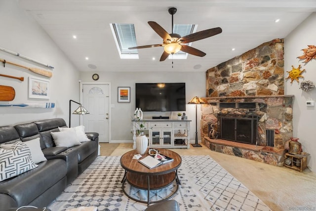 living room featuring ceiling fan, light colored carpet, a fireplace, and vaulted ceiling with skylight