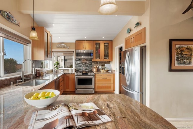 kitchen with pendant lighting, stainless steel appliances, sink, and light stone counters