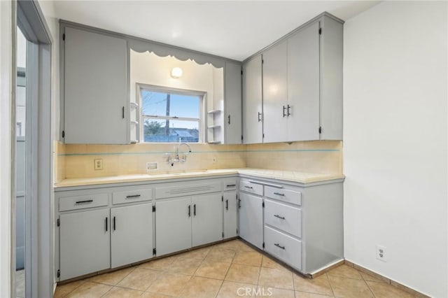 kitchen featuring light countertops, a sink, backsplash, and light tile patterned floors