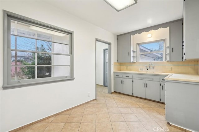 kitchen with light tile patterned floors, light countertops, backsplash, and a sink