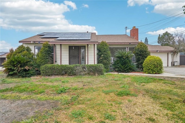 view of front of property with a front yard, roof mounted solar panels, a chimney, and an attached garage