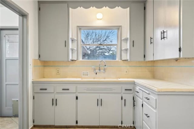 kitchen featuring tile countertops, tasteful backsplash, a sink, and white cabinets