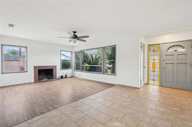 unfurnished living room featuring a brick fireplace, plenty of natural light, visible vents, and light wood finished floors