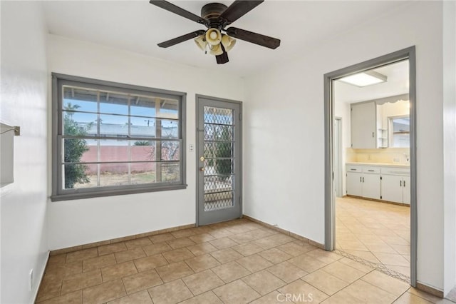 doorway with light tile patterned floors, ceiling fan, and baseboards