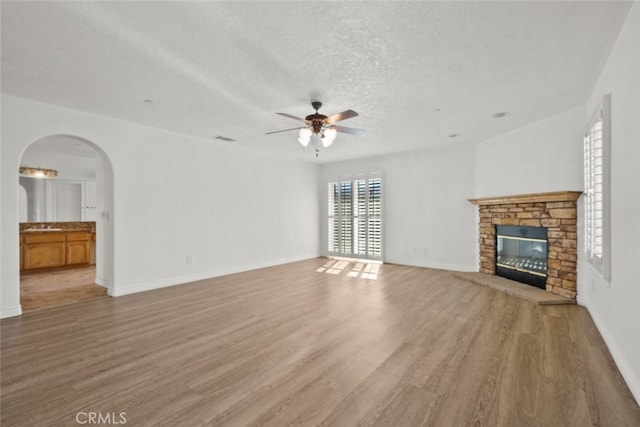 unfurnished living room with light hardwood / wood-style flooring, ceiling fan, a fireplace, and a textured ceiling