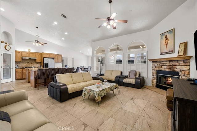 living room with ceiling fan, a stone fireplace, and high vaulted ceiling