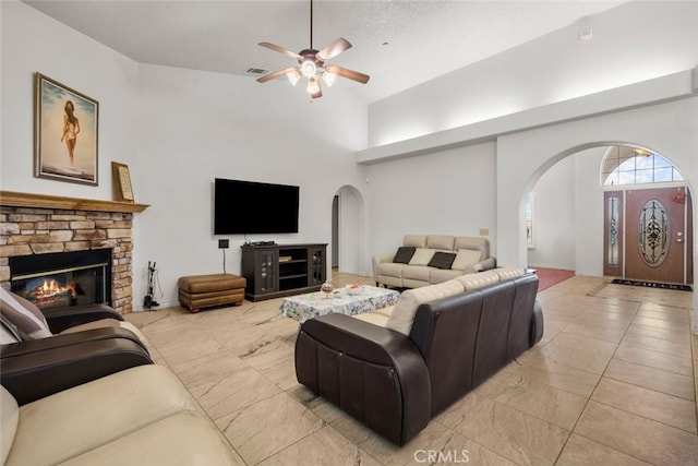 living room featuring ceiling fan, a towering ceiling, and a fireplace