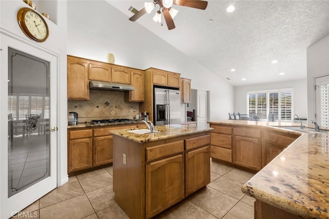 kitchen with appliances with stainless steel finishes, a center island with sink, light stone counters, and light tile patterned floors