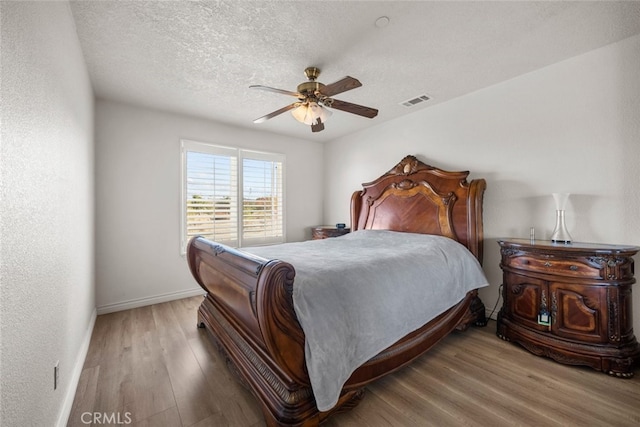 bedroom with ceiling fan, wood-type flooring, and a textured ceiling