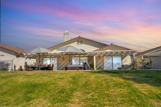 back house at dusk featuring a hot tub, a yard, and a pergola