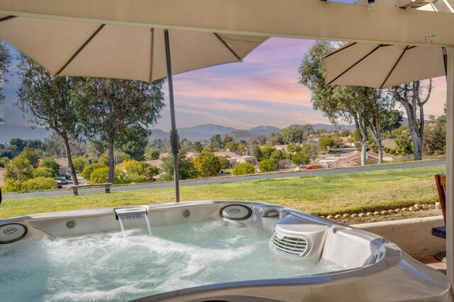 pool at dusk featuring a hot tub, a mountain view, and a yard