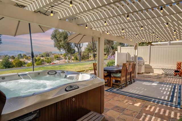 patio terrace at dusk with area for grilling, a mountain view, a pergola, and a hot tub